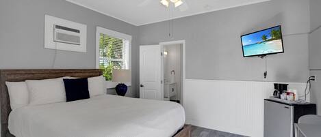 A bedroom with a bed, a desk, a TV, and a ceiling fan.