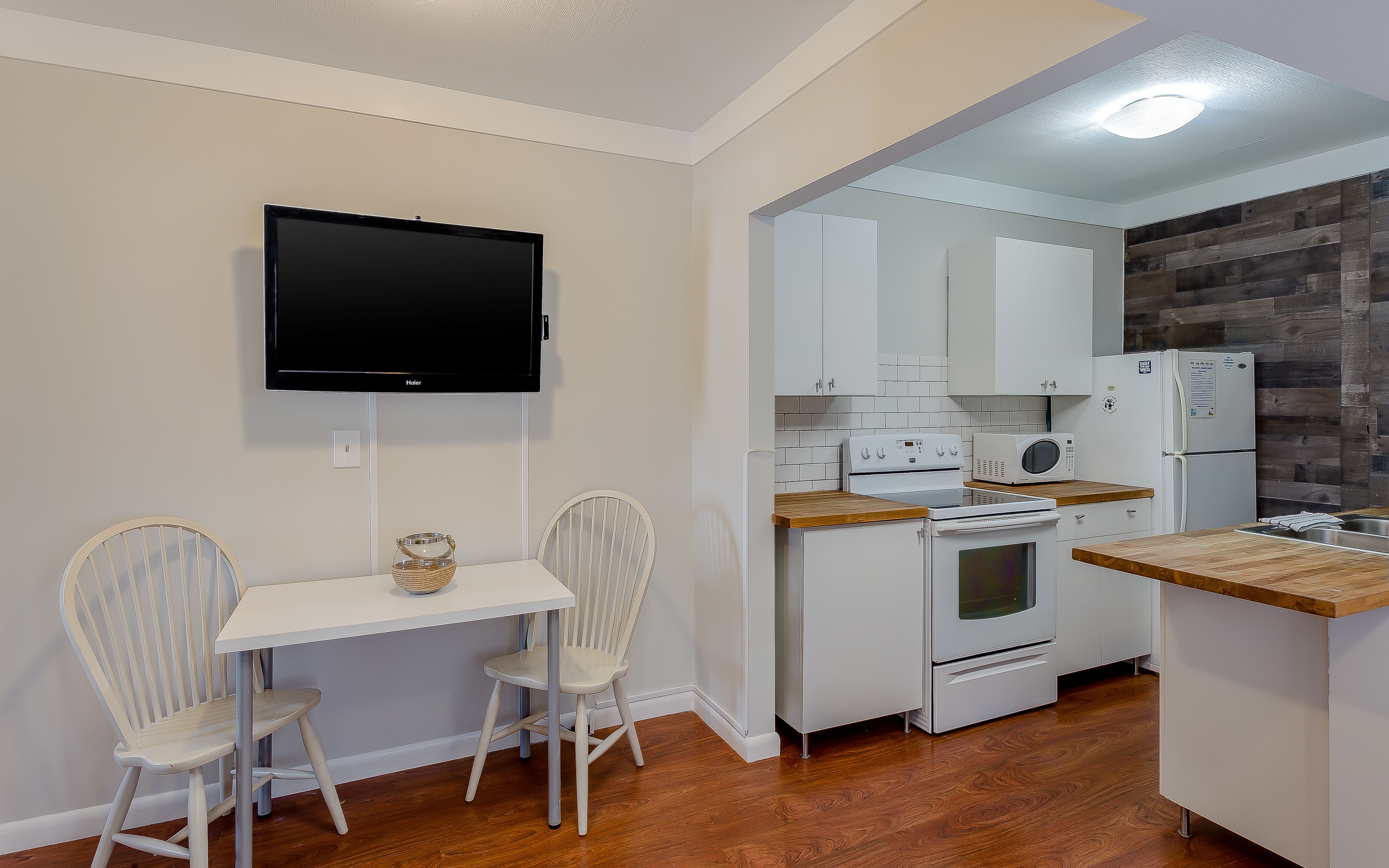 A compact kitchen with white cabinets, a microwave, a stove, and a flat-screen TV mounted on the wall.