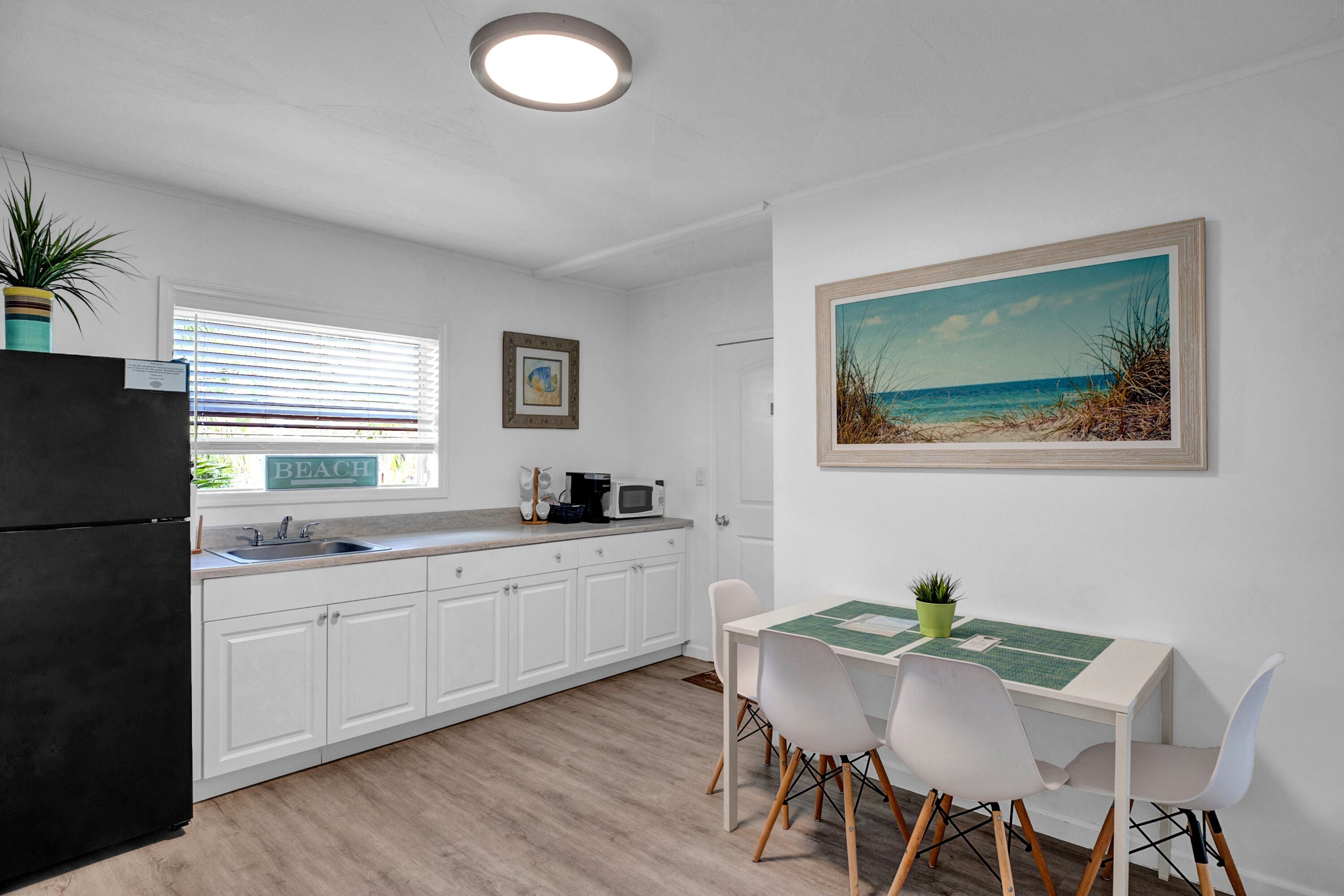 A modern kitchen with white cabinets, a black refrigerator, and a dining area with a table and chairs.