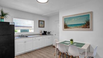 A modern kitchen with white cabinets, a black refrigerator, and a dining area with a table and chairs.