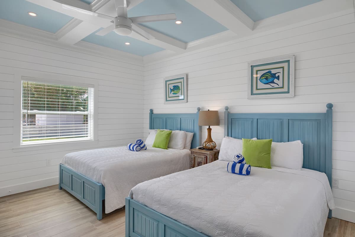 A bedroom with two beds, a ceiling fan, and a window with blinds.