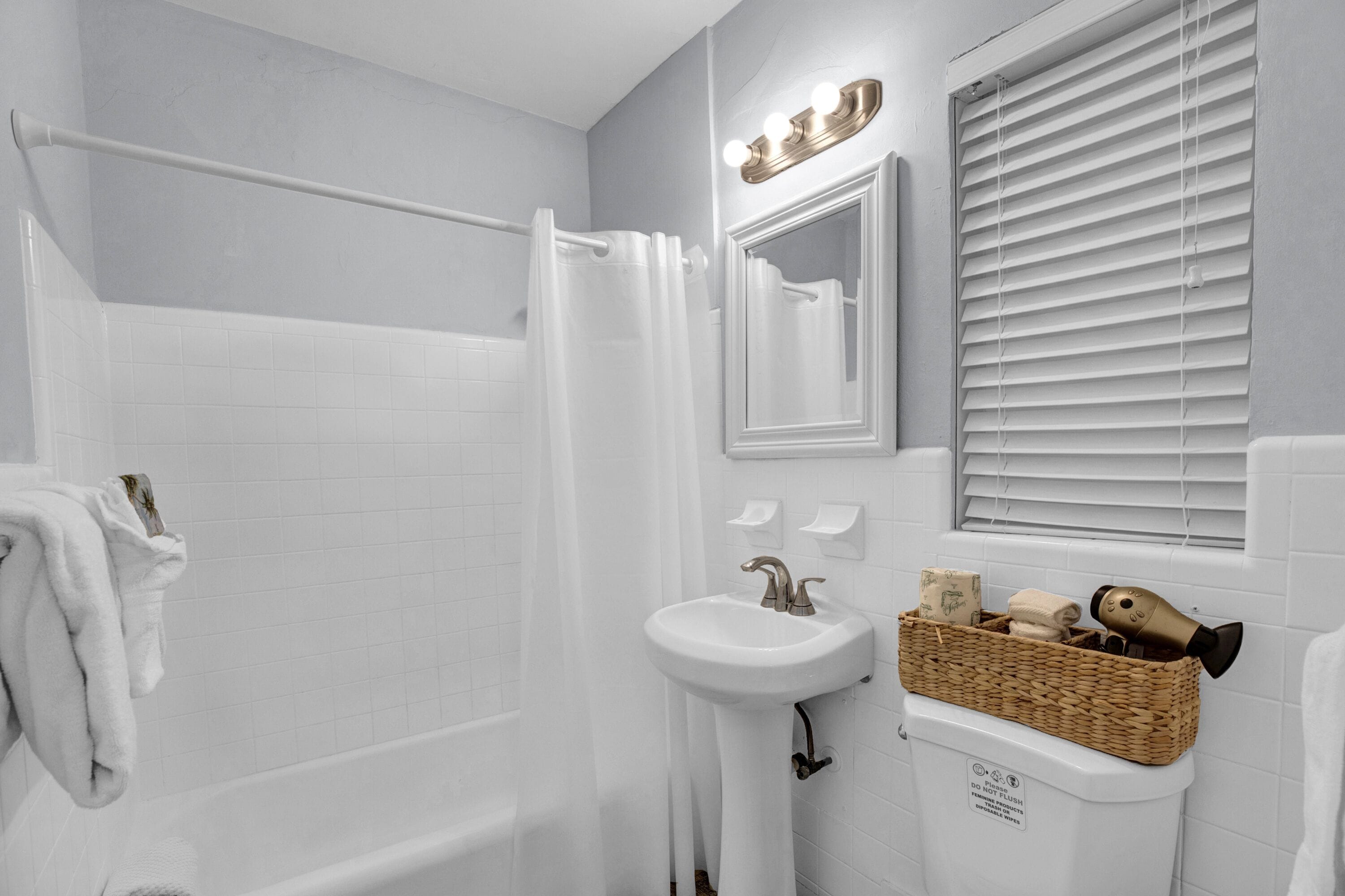 A bathroom with a bathtub, a sink, a mirror, and a window with blinds.