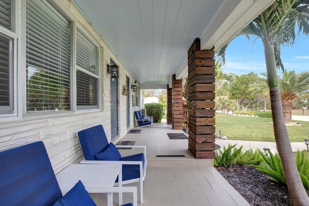 A covered porch with white railings, blue cushioned chairs, and a palm tree.
