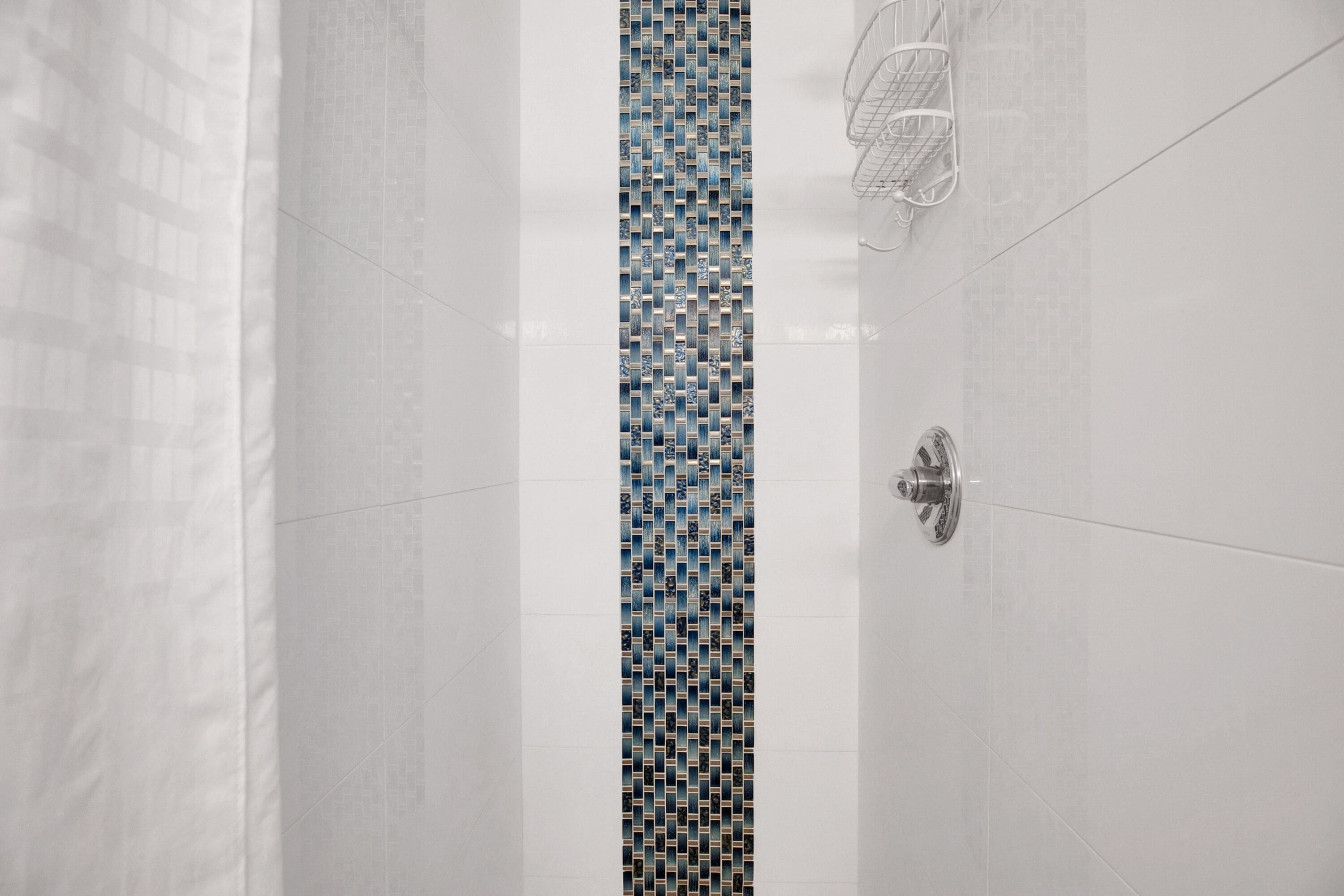 Un baño moderno con azulejos blancos, una pared decorativa de azulejos estampados y una ducha con un estante metálico.