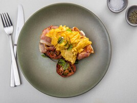 Lautasella on munakokkelia, pekonia ja tomaatteja, ja lautanen on vihreä.