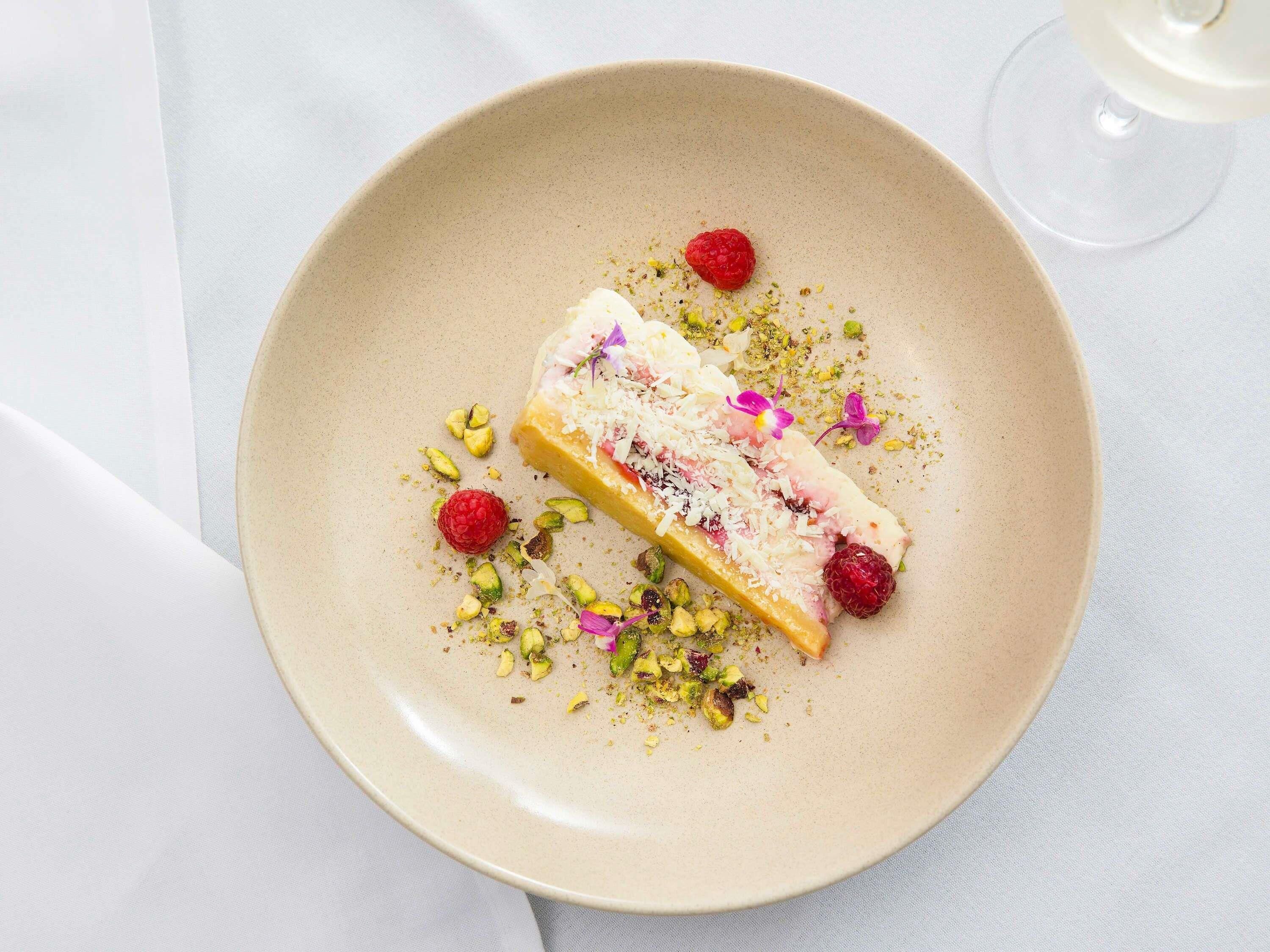 A dessert on a plate with pistachios and raspberries.