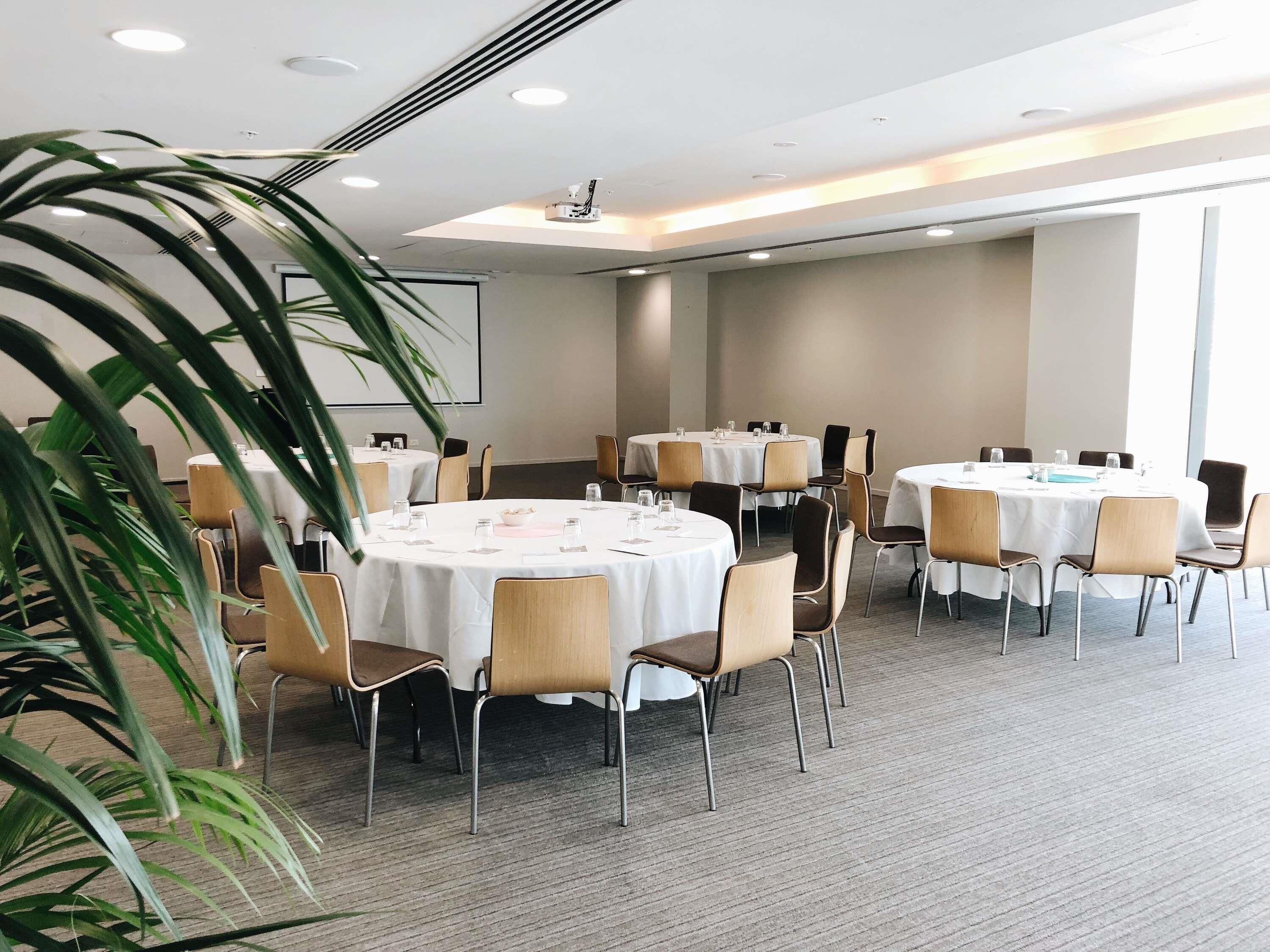 A conference room with round tables, chairs, and a projector screen.