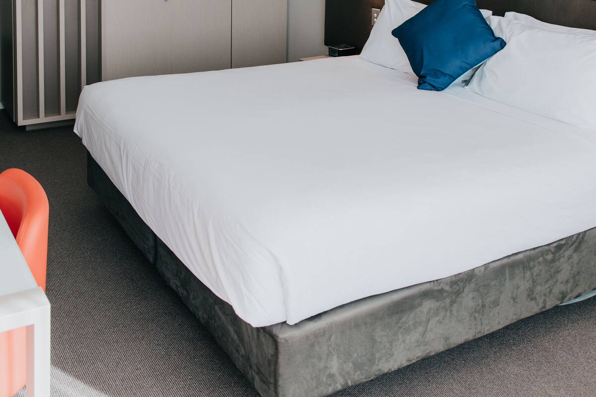 A hotel room with a large bed, a wardrobe, a nightstand, and a lamp.