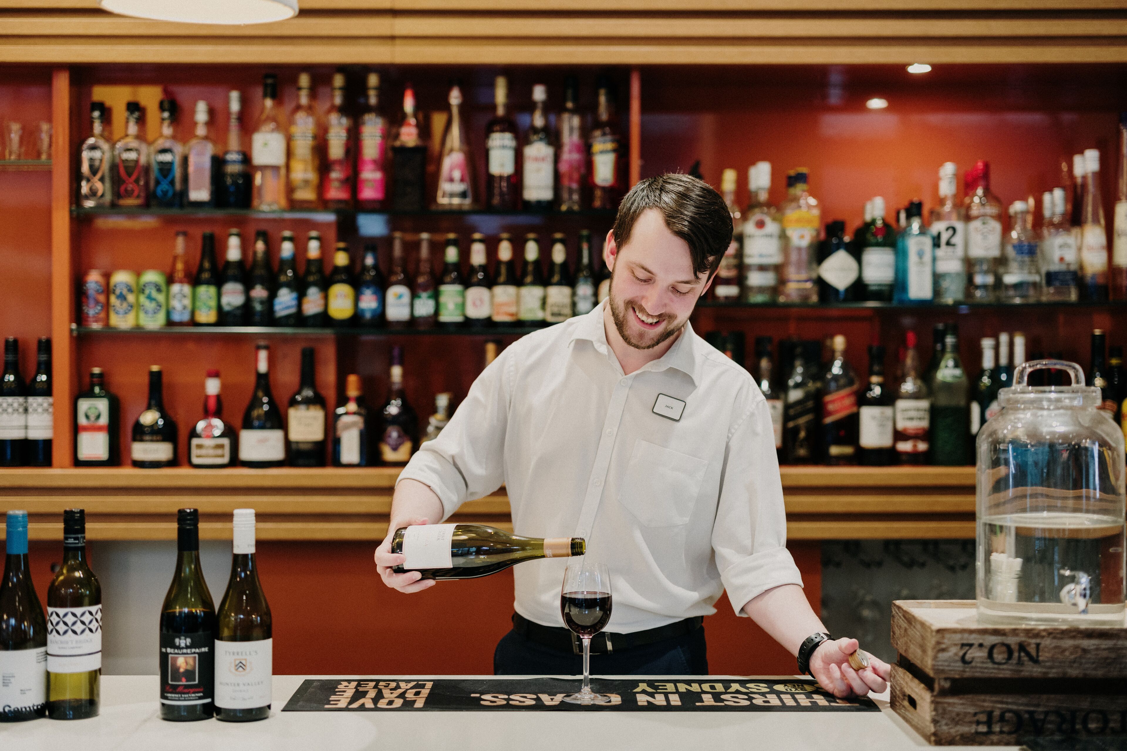 A bar area with a variety of liquor bottles on shelves and a person pouring wine into a glass.
