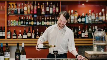 A bar area with a variety of liquor bottles on shelves and a person pouring wine into a glass.