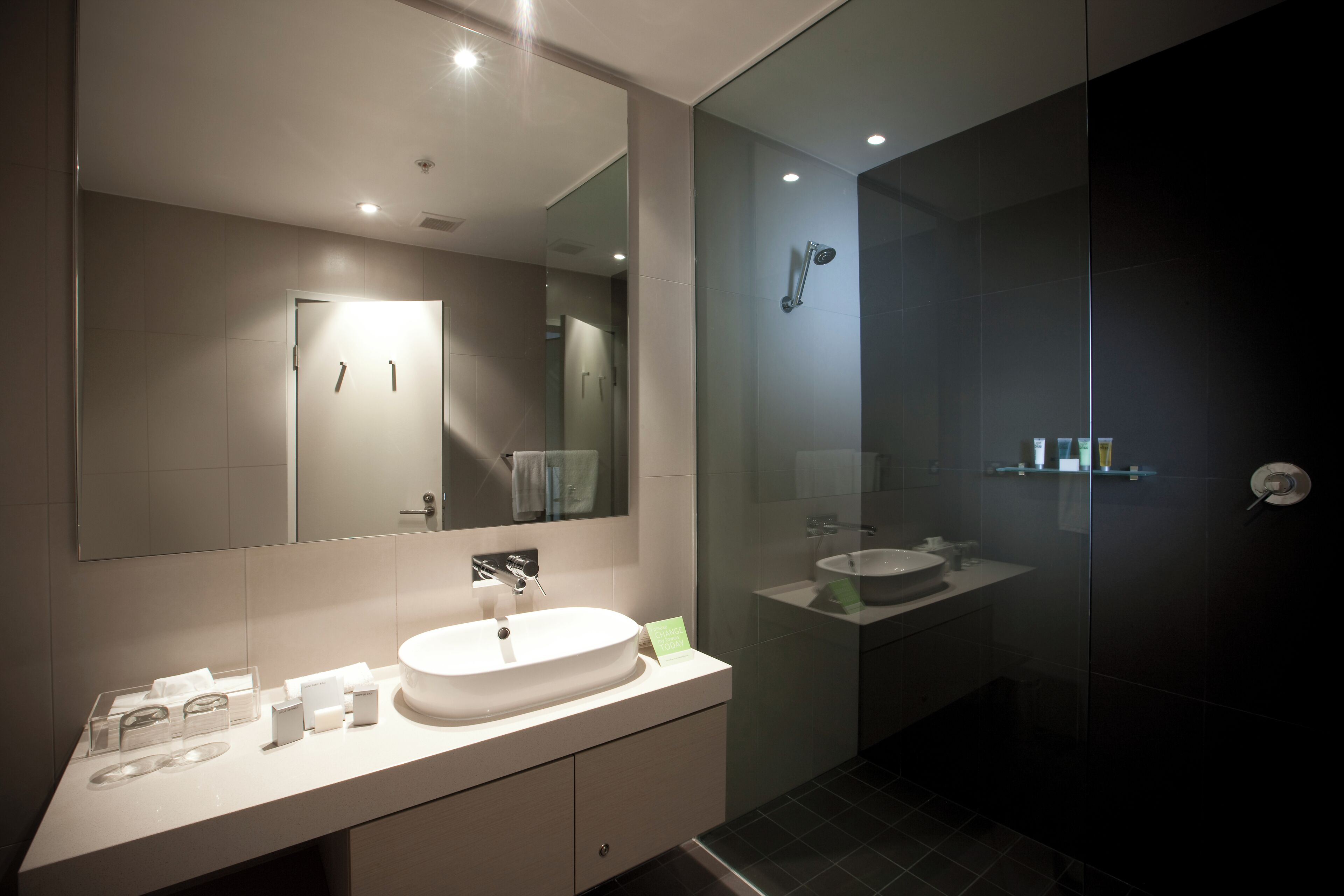 A modern bathroom with a large mirror, a vanity with a sink, and a glass shower enclosure.