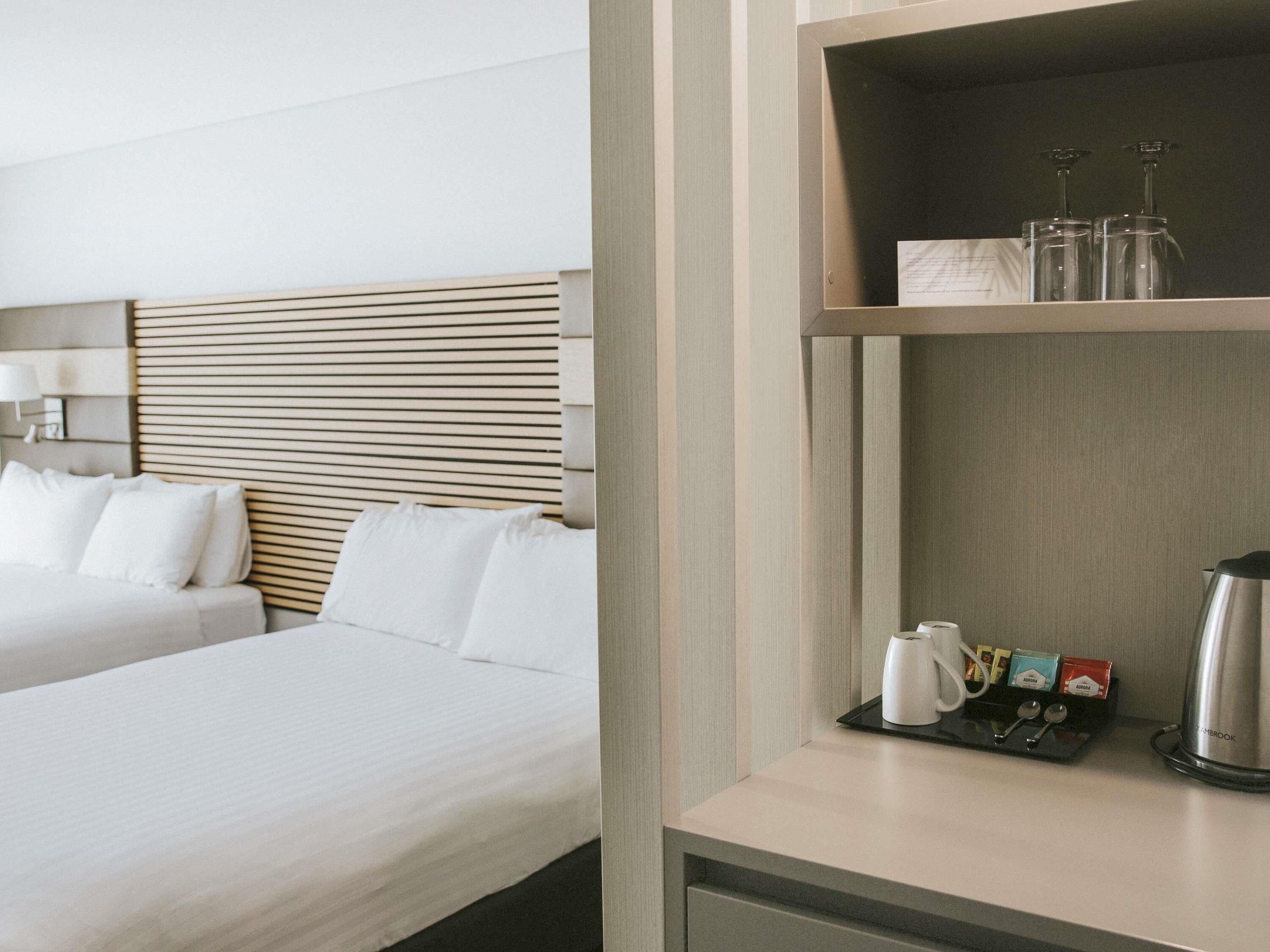 Habitación de hotel con dos camas, una mesita de noche con cafetera, bolsitas de té y vasos.