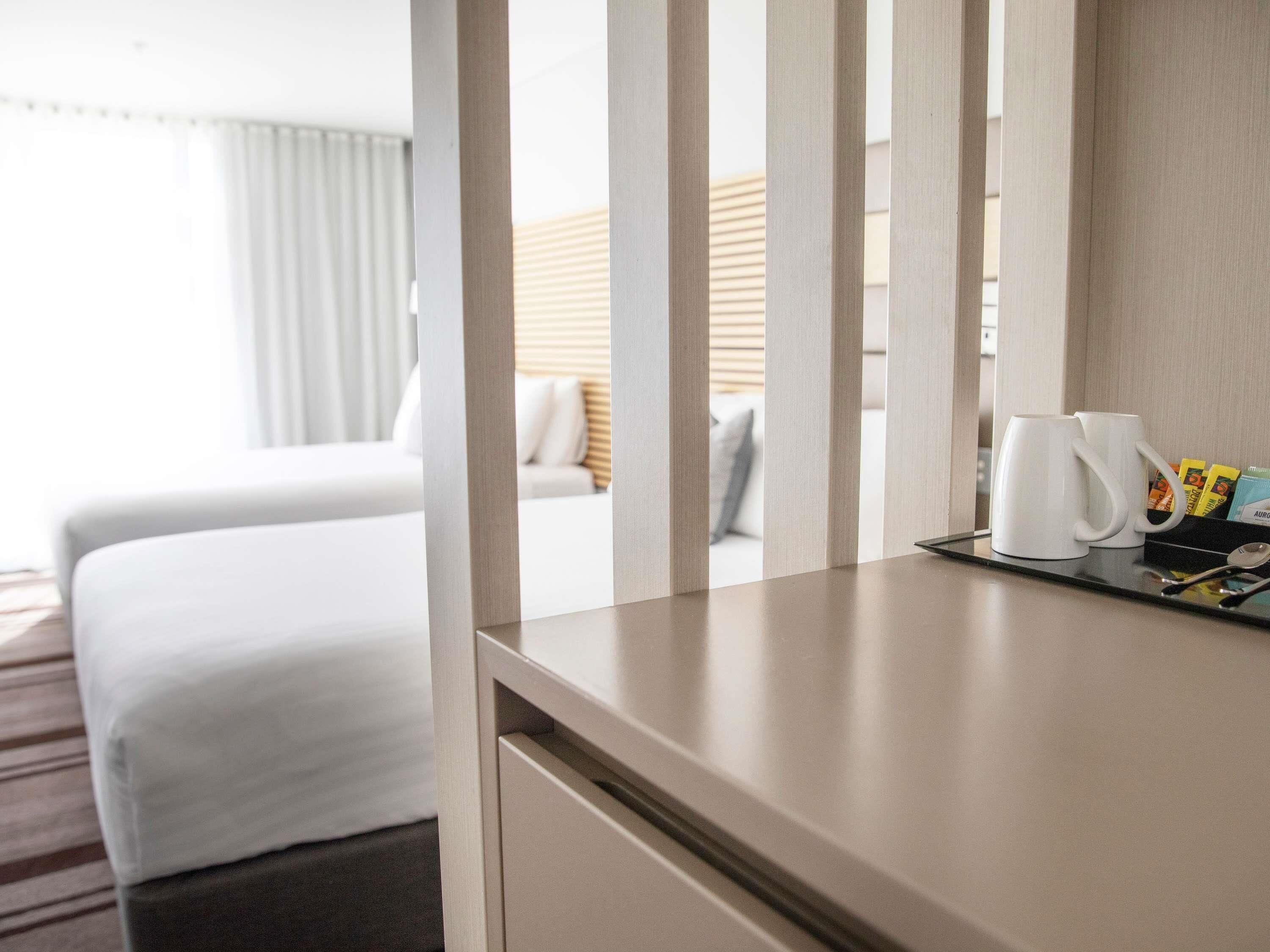 A hotel room with a bed, a bedside table with a coffee maker, and a tray with toiletries.