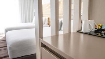 A hotel room with a bed, a bedside table with a coffee maker, and a tray with toiletries.
