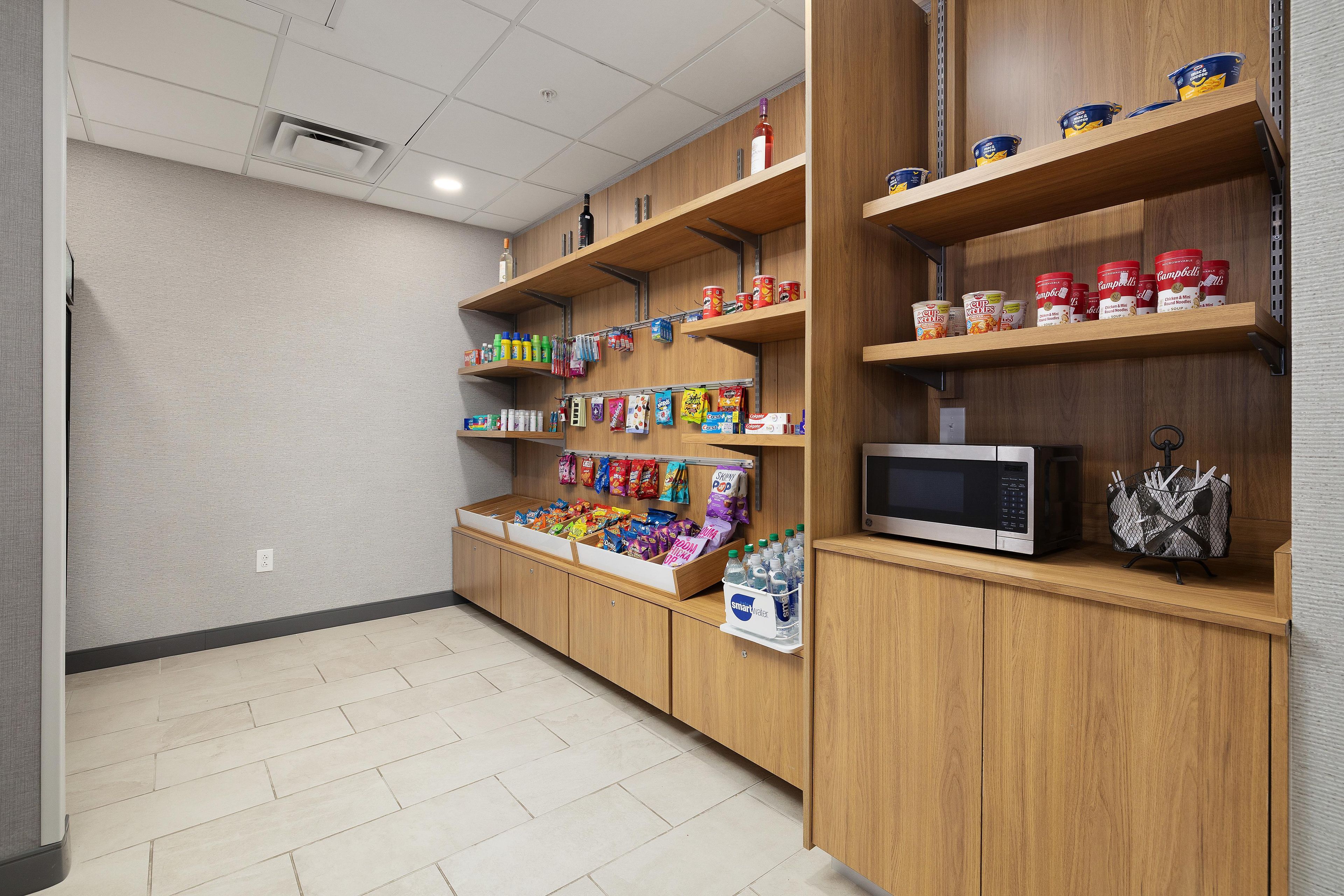 A kitchenette area with wooden cabinets, a microwave, and various food items on shelves.