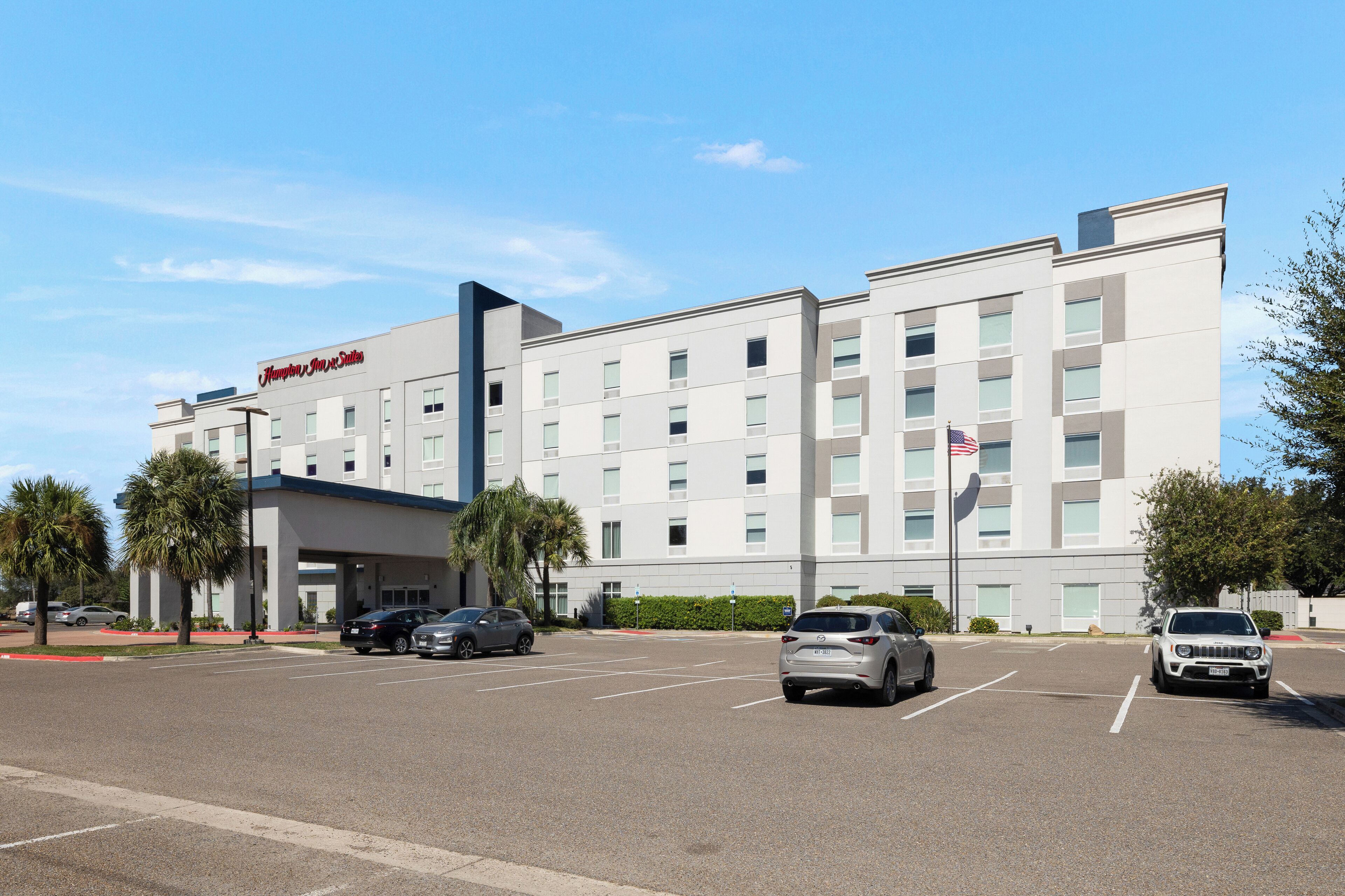 A modern hotel with a flat facade, multiple floors, and a parking lot with several cars.