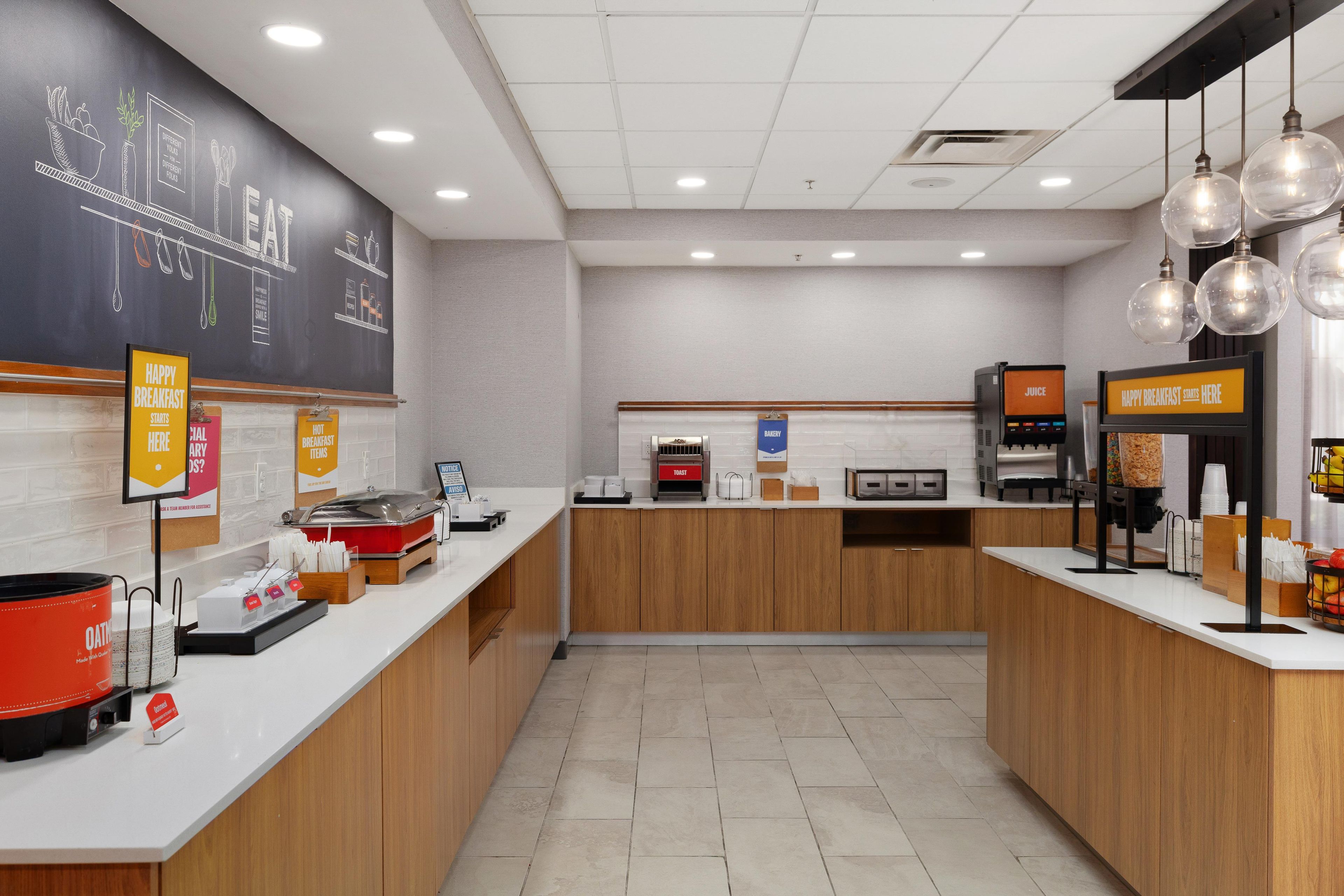 A modern breakfast area with a chalkboard menu, juice dispenser, and a coffee machine.