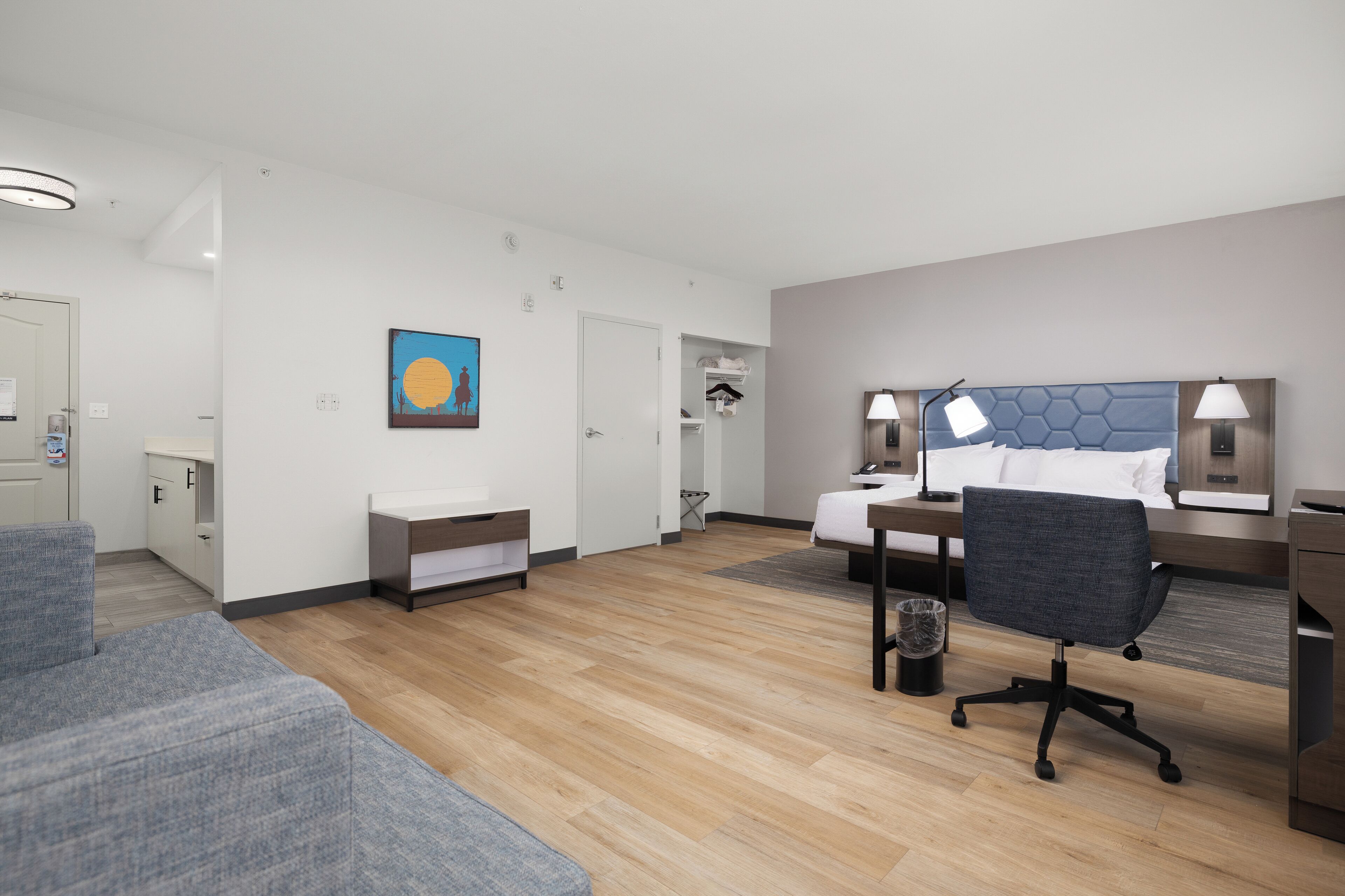 Quarto de hotel moderno com cama, escrivaninha, cadeira e um pequeno espaço de estar.