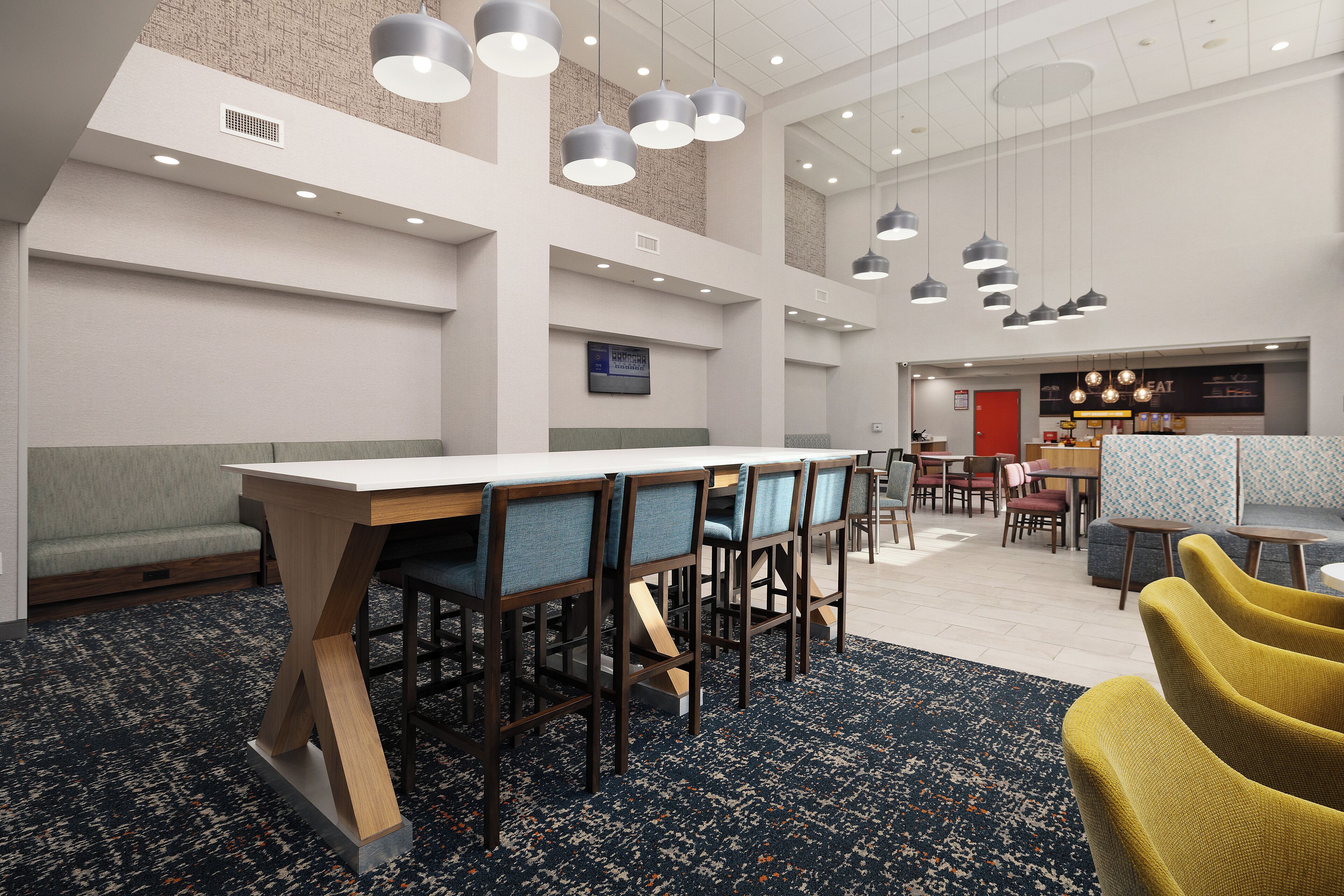 Een moderne hotel lobby met een lange receptiebalie, meerdere zithoeken en een zichtbare etage voor eten.
