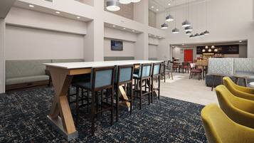 Een moderne hotel lobby met een lange receptiebalie, meerdere zithoeken en een zichtbare etage voor eten.