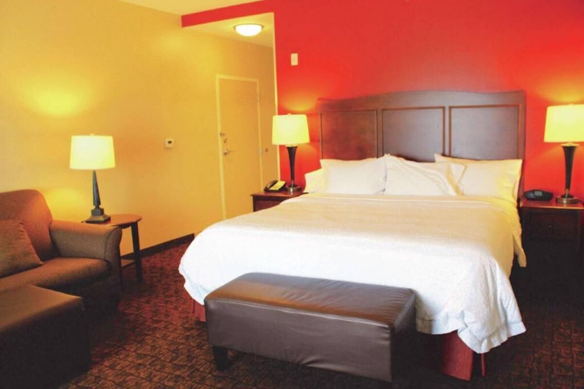 A hotel room with a large bed, two bedside tables with lamps, a chair, and a door.