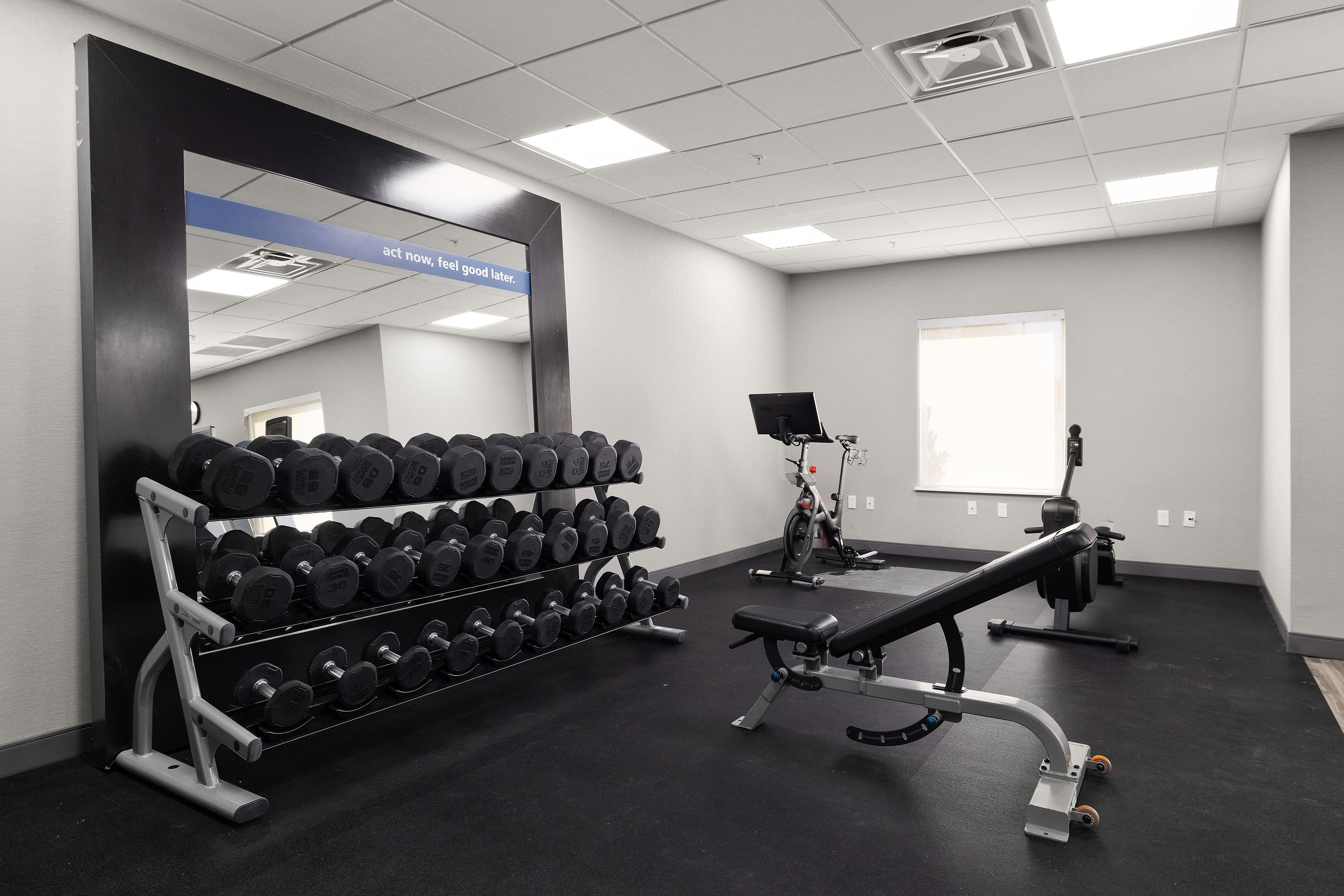 A gym with a mirrored wall, dumbbells, a bench press, and a stationary bike.