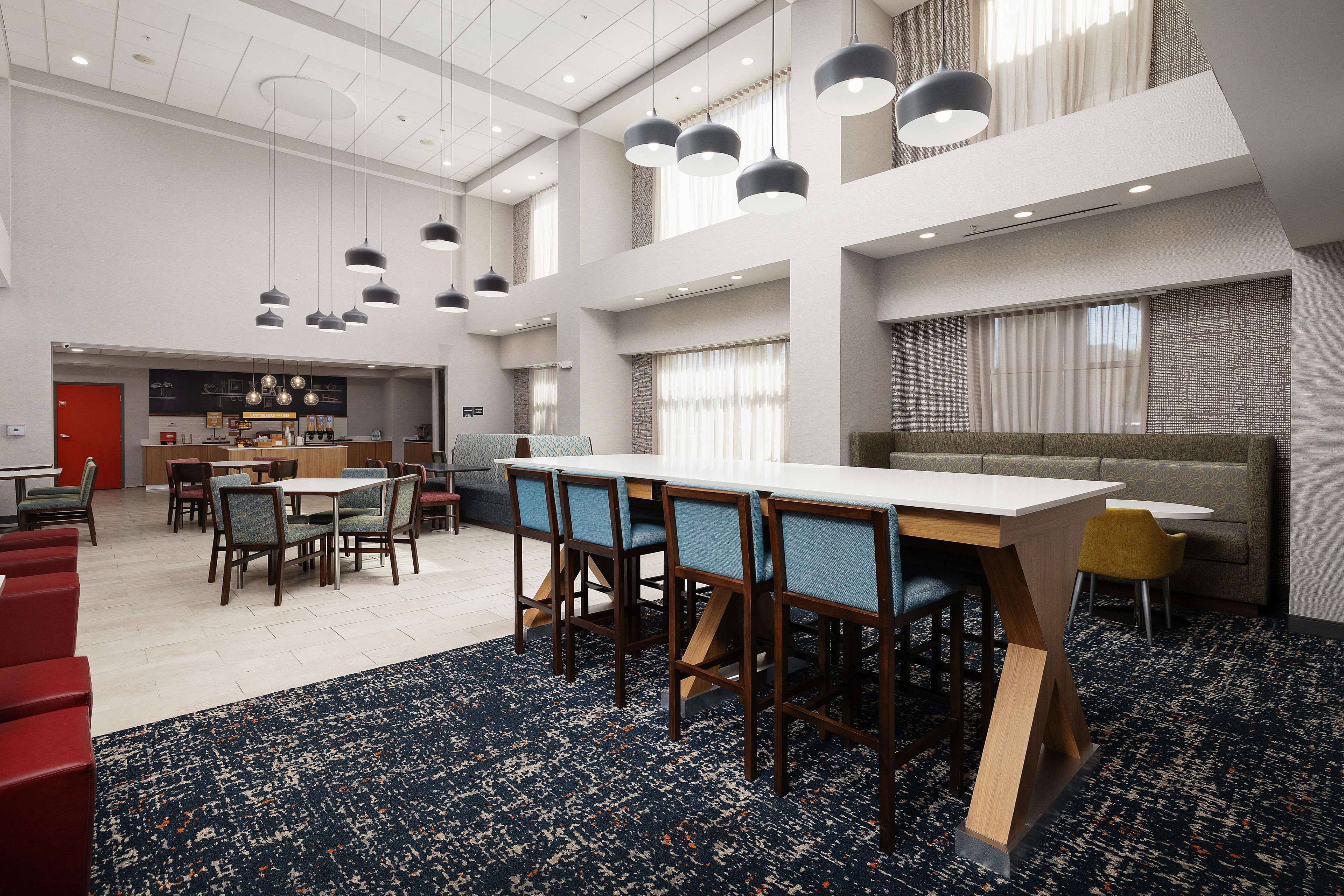 A spacious hotel lobby with a high ceiling, multiple seating areas, and a central dining table.