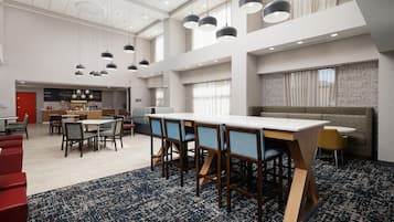 Un amplio vestíbulo de hotel con techo alto, varias zonas de estar y una mesa de comedor central.