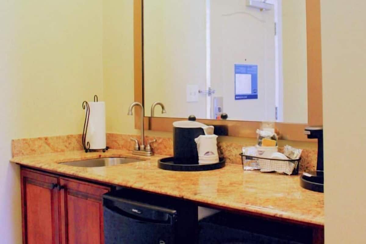 A bathroom with a sink, mirror, towel rack, and a coffee maker.