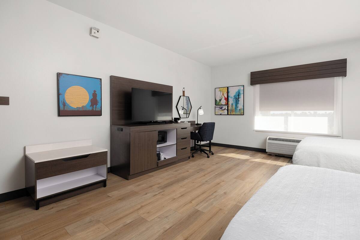 A hotel room with a bed, a desk with a chair, a TV, and artwork on the walls.
