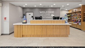 Eine Hotelrezeption mit einem Schild, auf dem 'Welcome to the Lone Star State' steht, einer Minibar und einem Selbstbedienungskiosk.