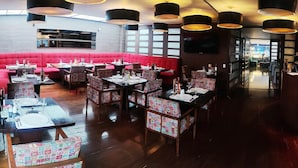 Un restaurante con asientos rojos tipo banca, sillas estampadas y varias mesas de comedor.
