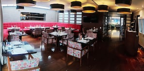 Un restaurante con asientos rojos tipo banca, sillas estampadas y varias mesas de comedor.