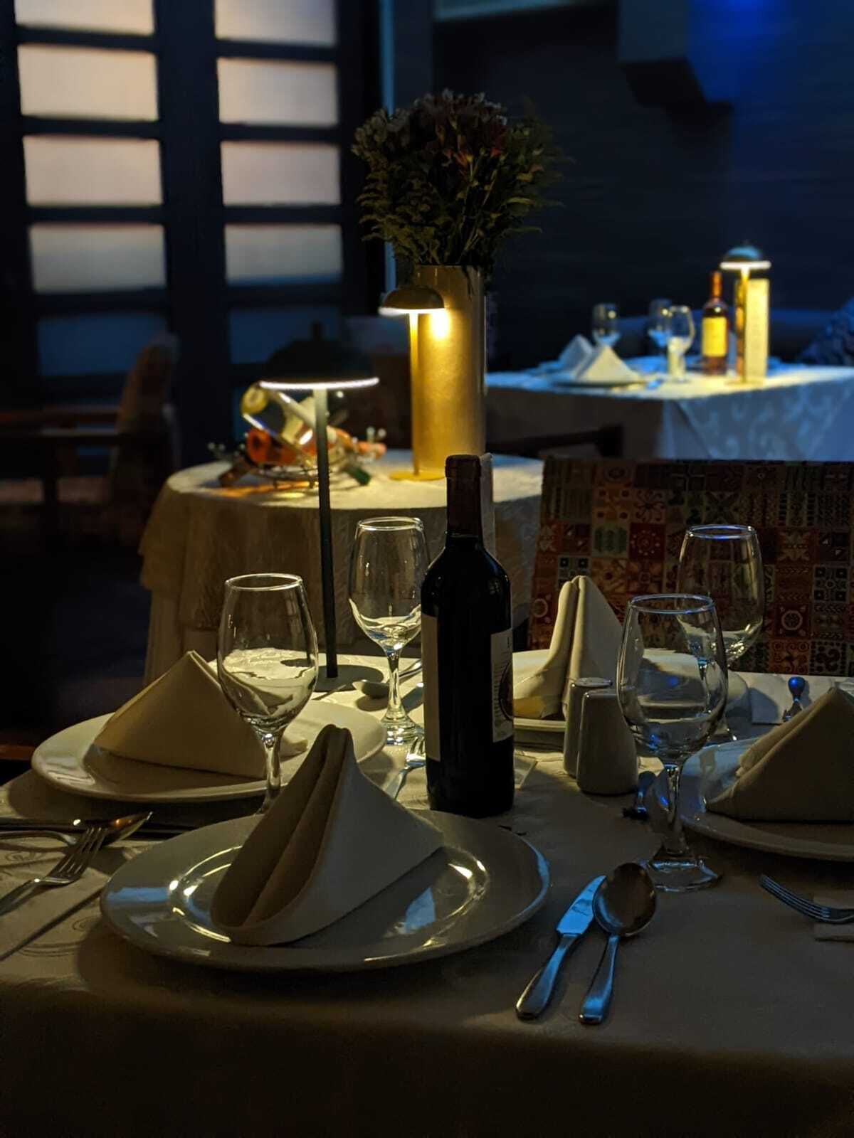 Une table dressée pour un dîner à deux, avec une bouteille de vin, des verres et un vase de fleurs.
