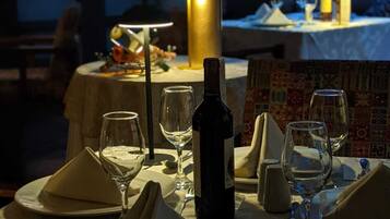 Mesa de comedor lista para dos personas, con una botella de vino, copas y un jarrón de flores.