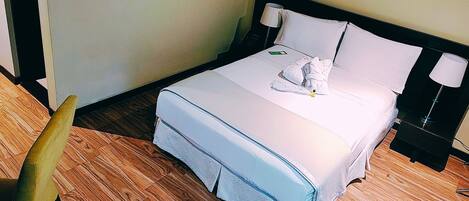 Habitación de hotel con cama, lámparas de noche, mesita de noche y suelo de madera.