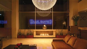 A modern lounge area with a fireplace, a sofa, a coffee table with flowers, and a neon sign reading "BLUE SUITES". - Blue Suites Hotel (Bogotá)