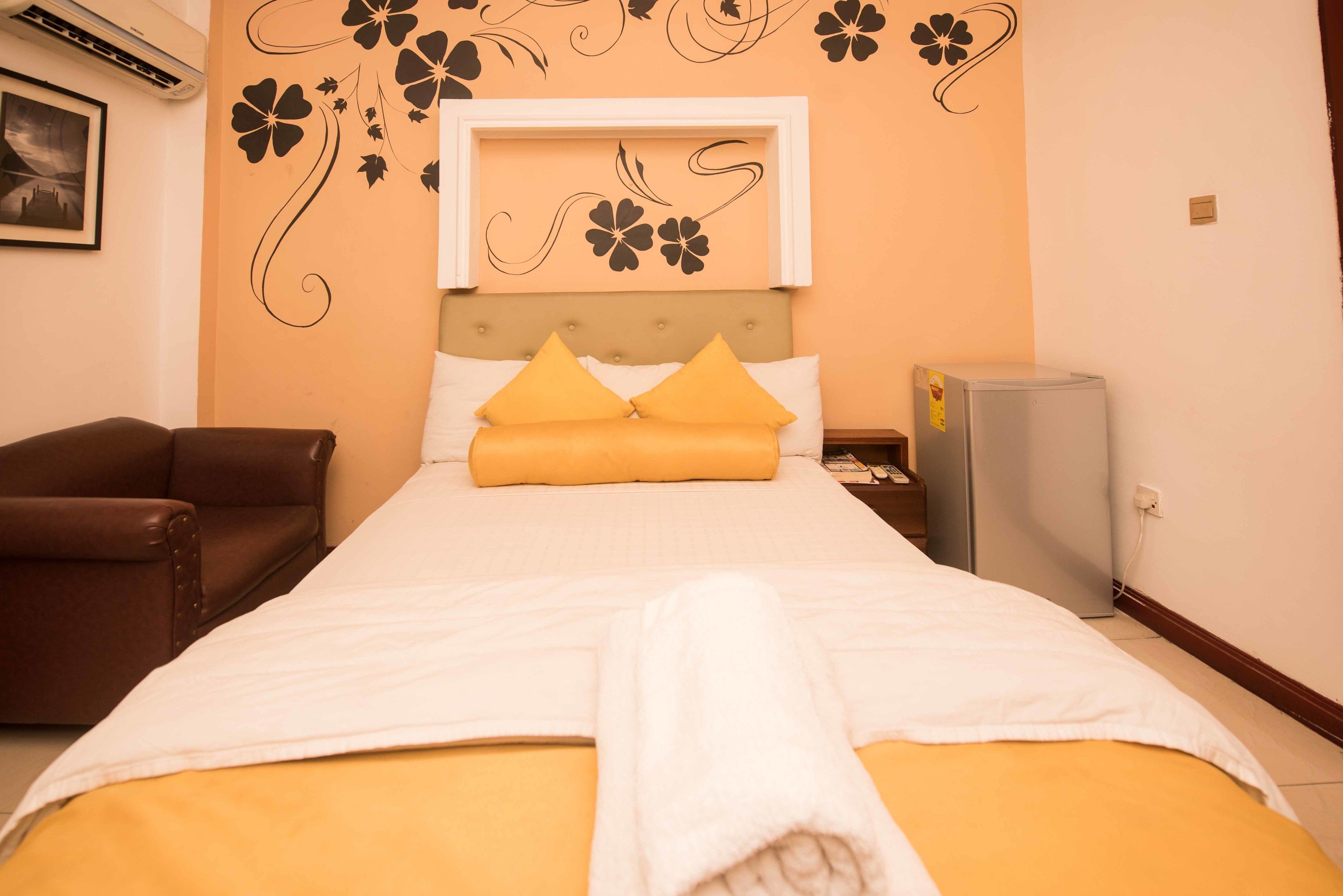Habitación de hotel con cama, un sillón de cuero marrón, una mesita con lámpara y aire acondicionado instalado en la pared.