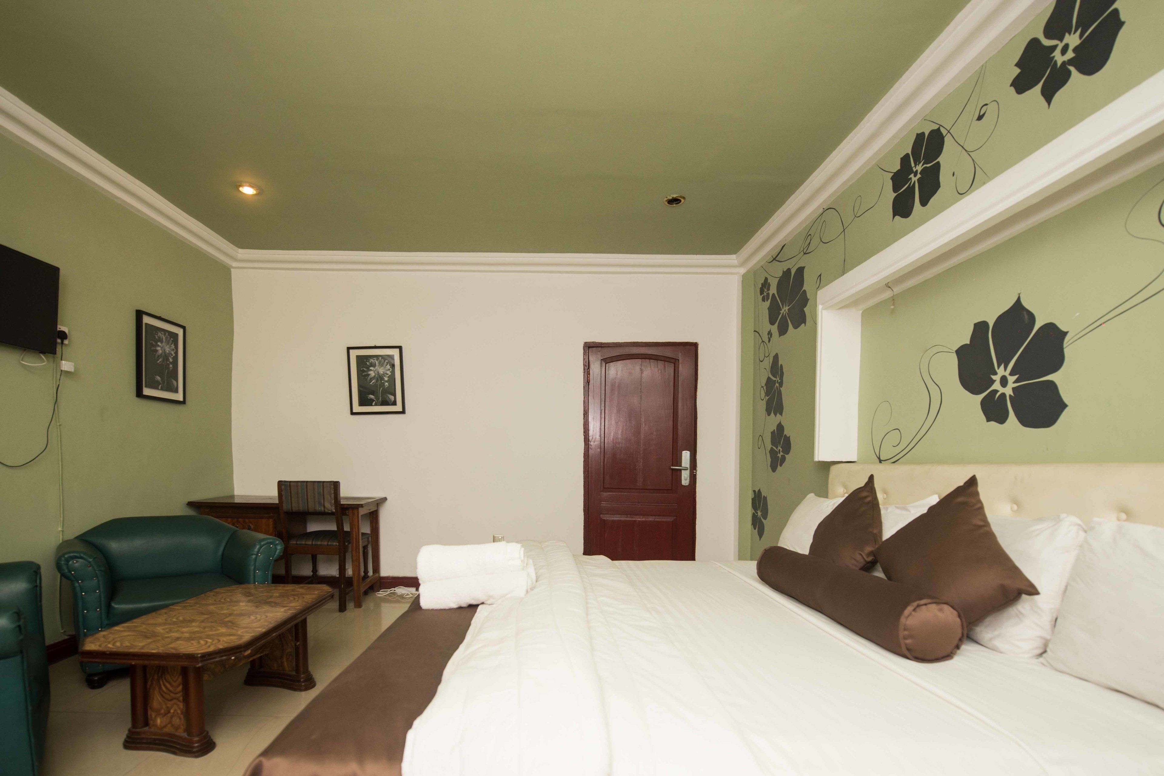 Una habitación de hotel con una cama, un sillón verde, una mesa de madera y un escritorio pequeño.