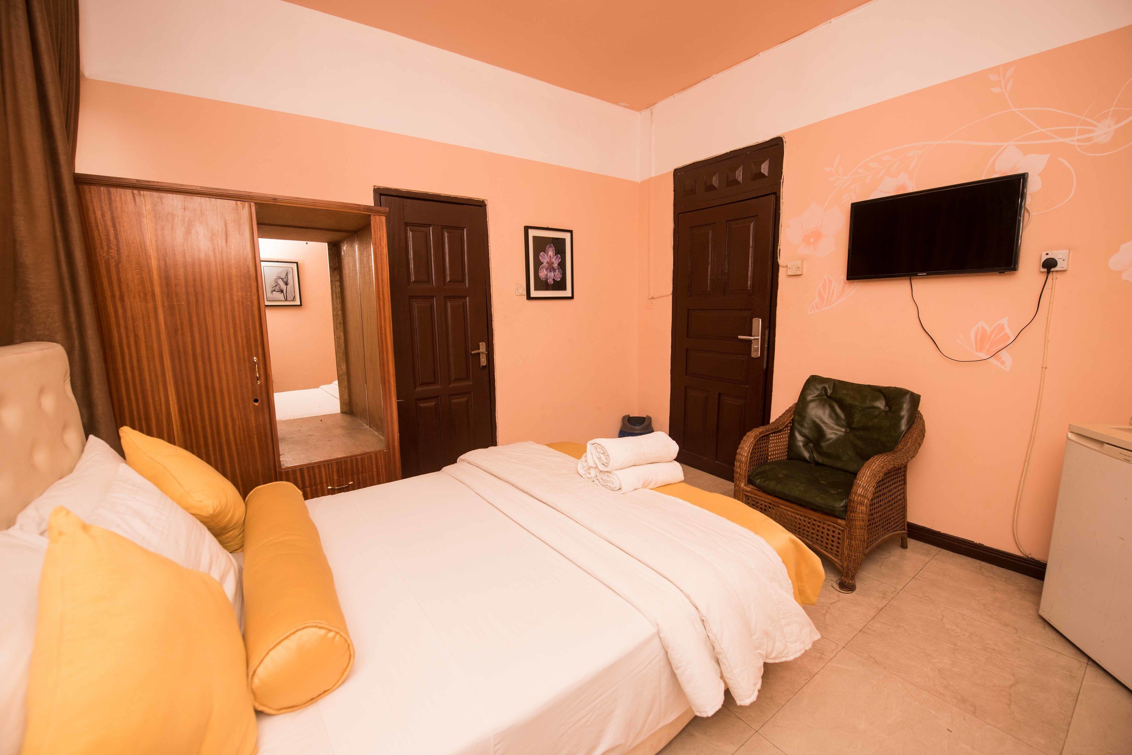 A hotel room with a bed, a chair, a television, and a wardrobe.