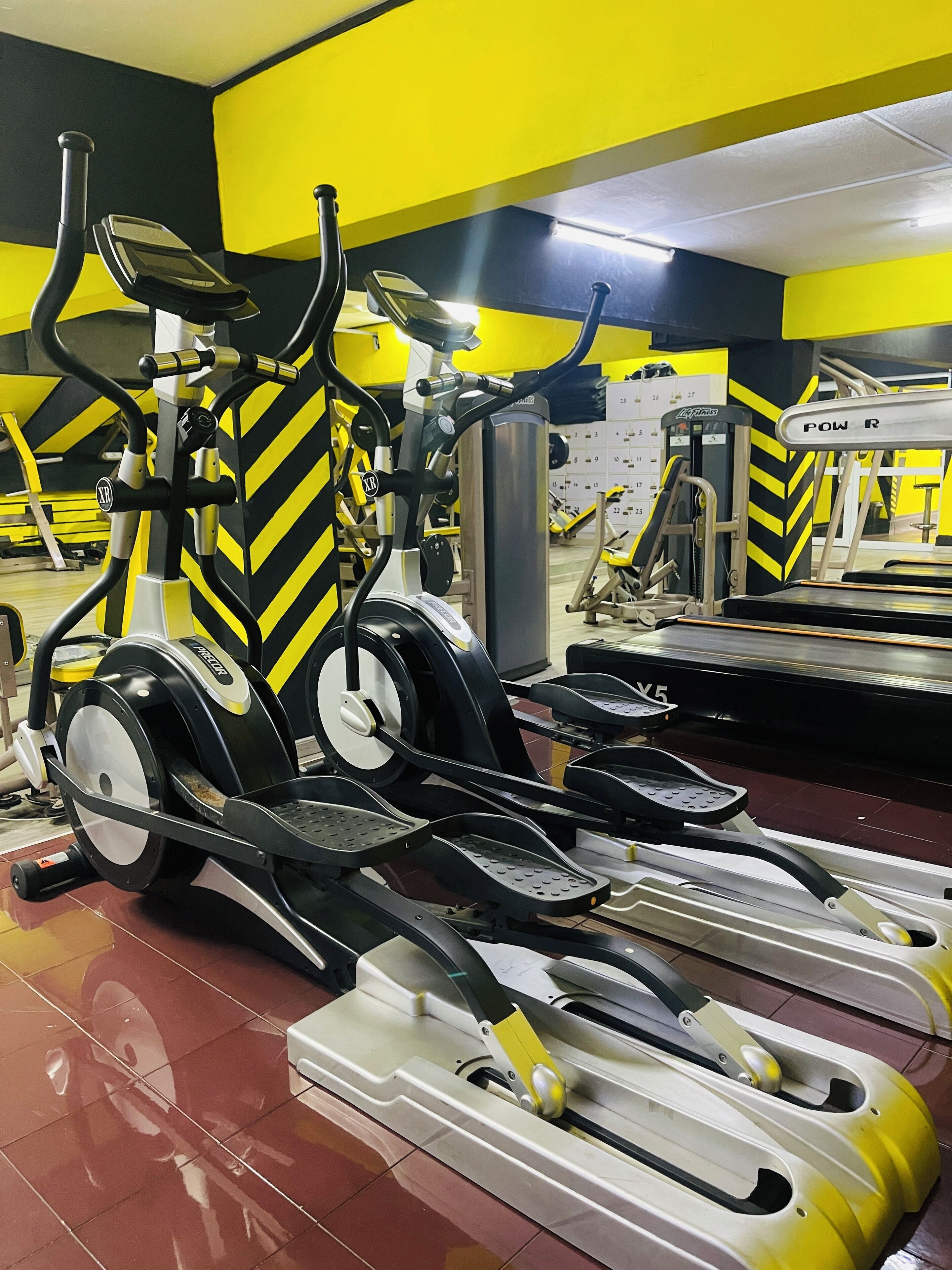 A gym with stationary bikes and treadmills, featuring yellow and black decor.