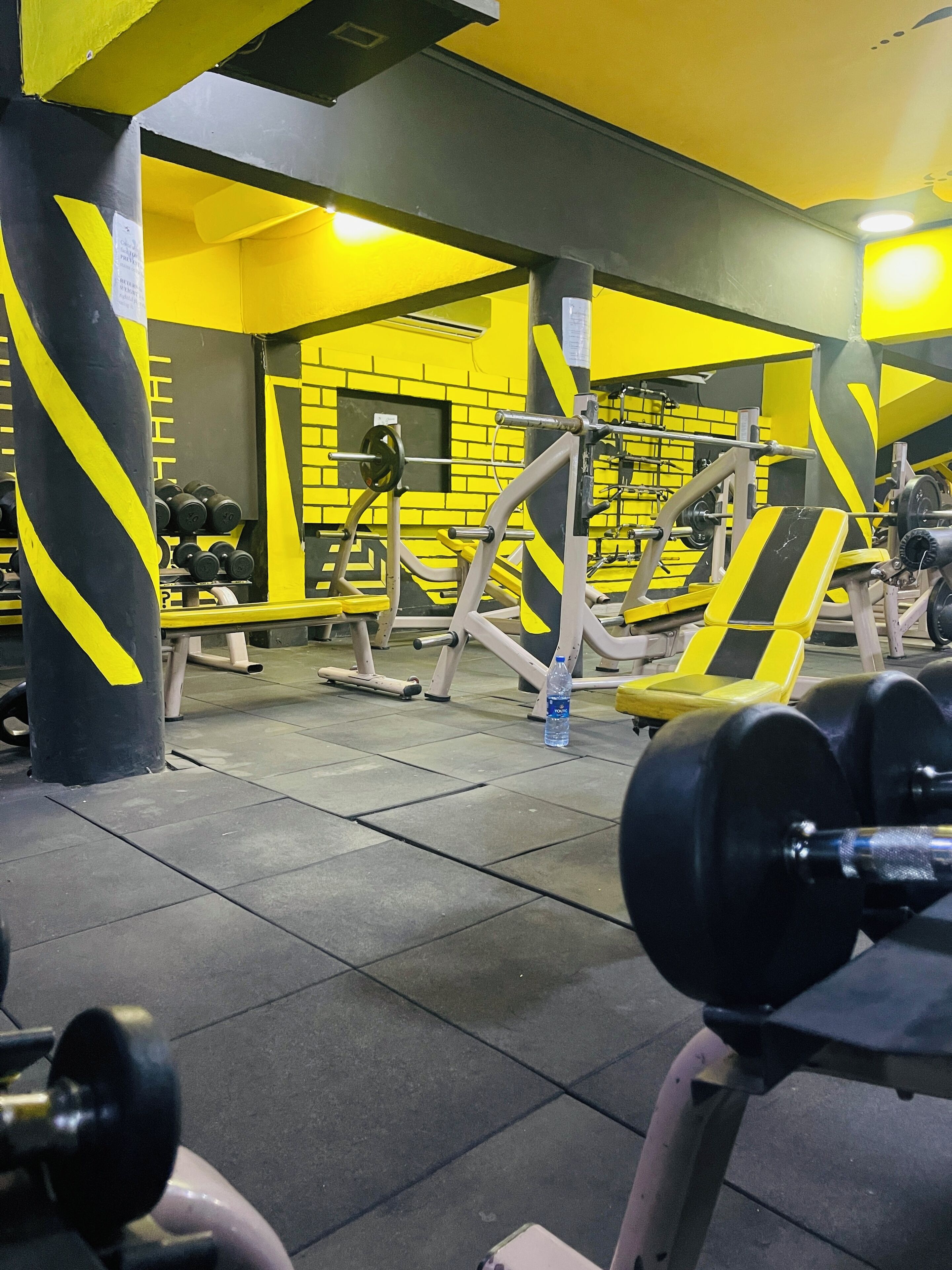 A gym with yellow and black decor, weightlifting equipment, and a bench.