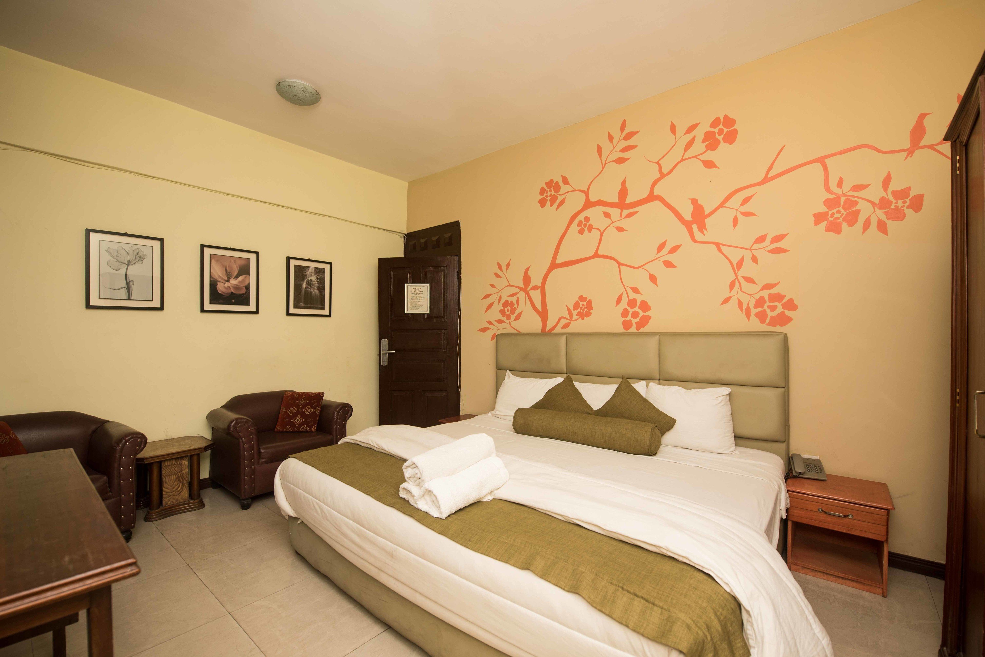 Een hotelkamer met een bed, twee fauteuils, een tafeltje en een nachtkastje.