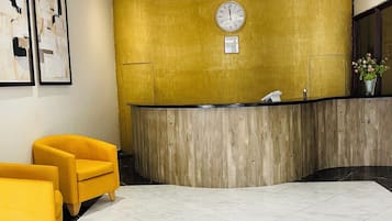 Ein Empfangsbereich mit einem Holzbüro, einer Uhr und zwei gelben Sessel.