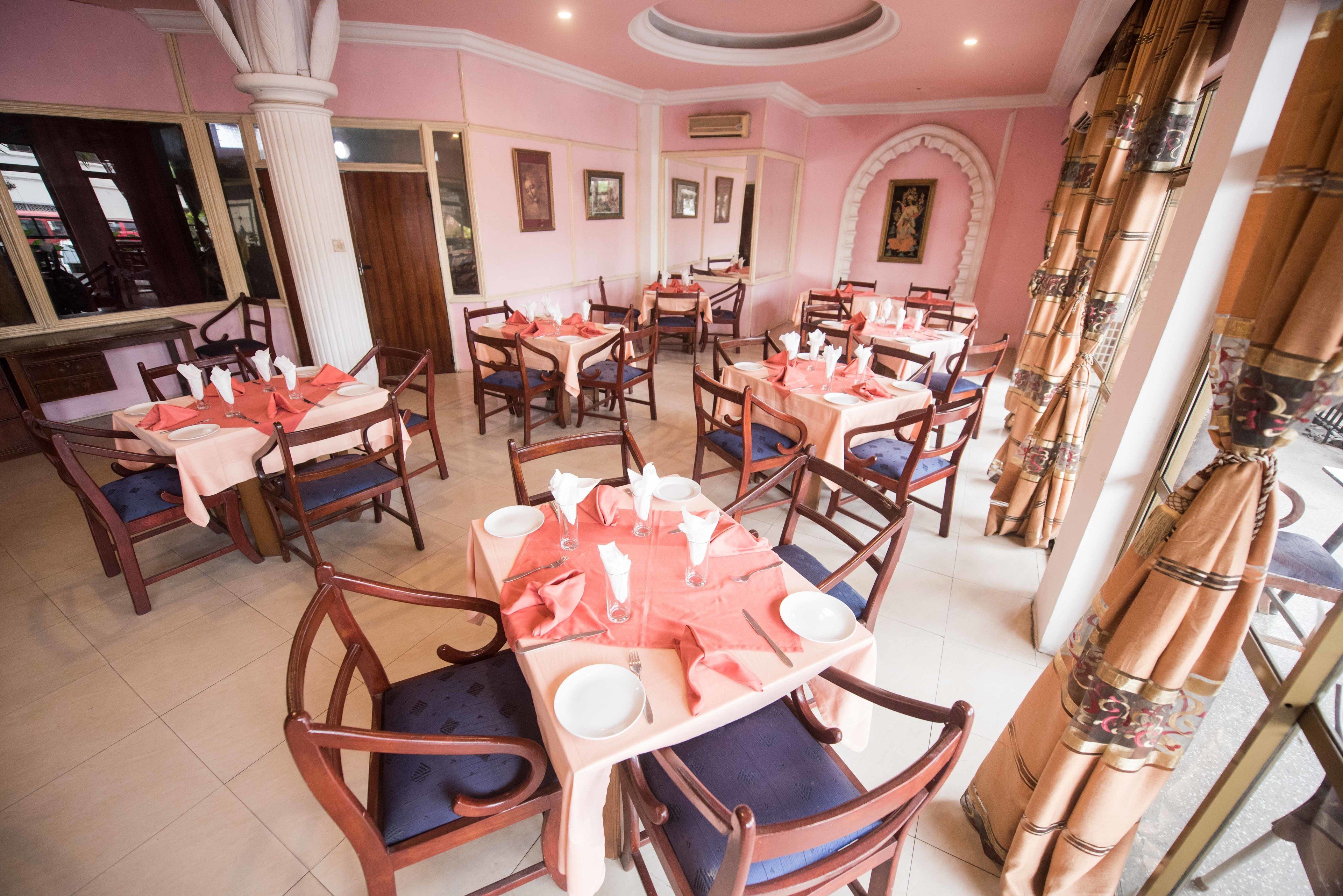 A dining area with tables set for four, each with blue cushioned chairs, pink tablecloths, and white napkins.