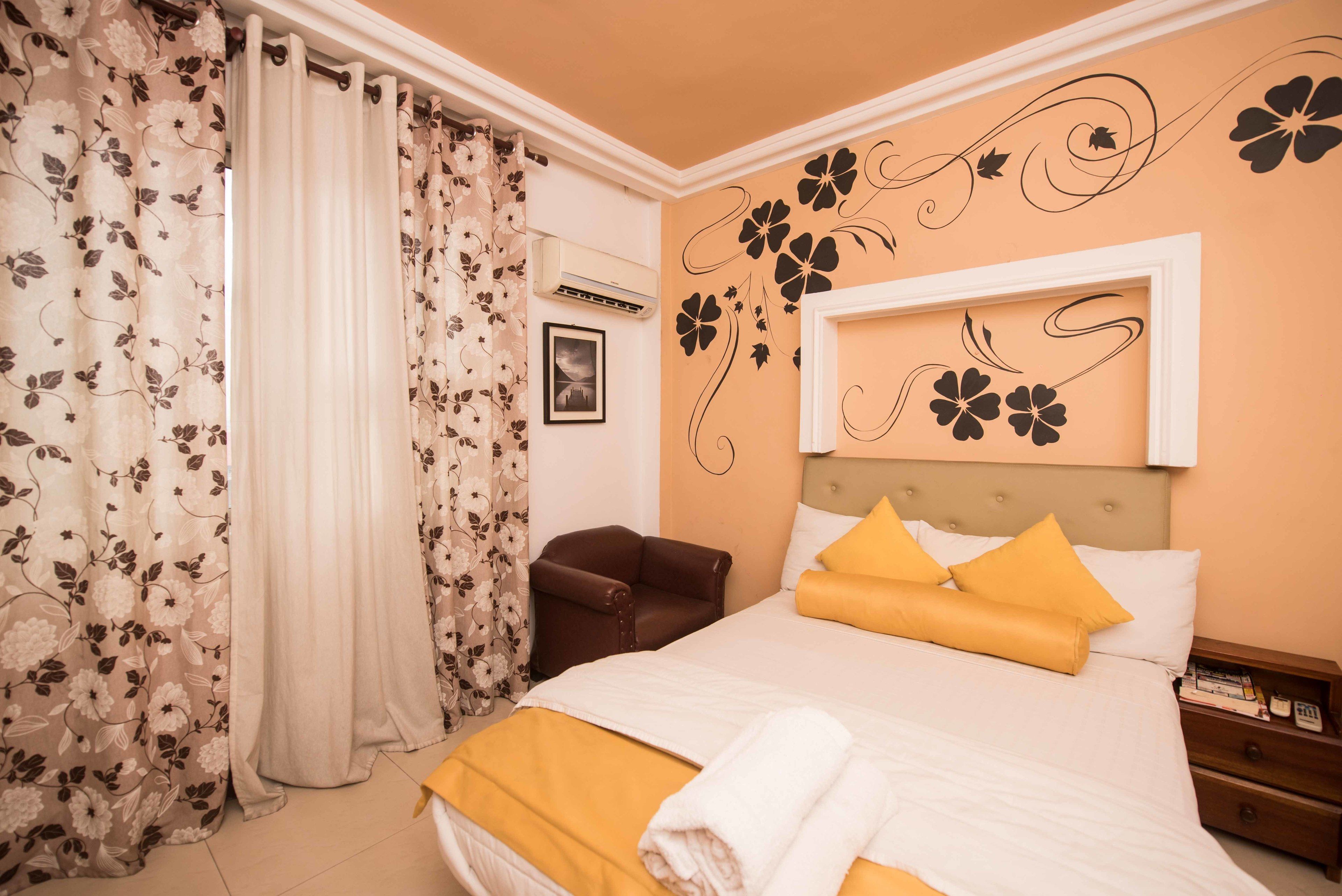 Une chambre d’hôtel avec un lit, une table de chevet, un fauteuil en cuir marron, un climatiseur fixé au mur et un tableau encadré accroché au mur.