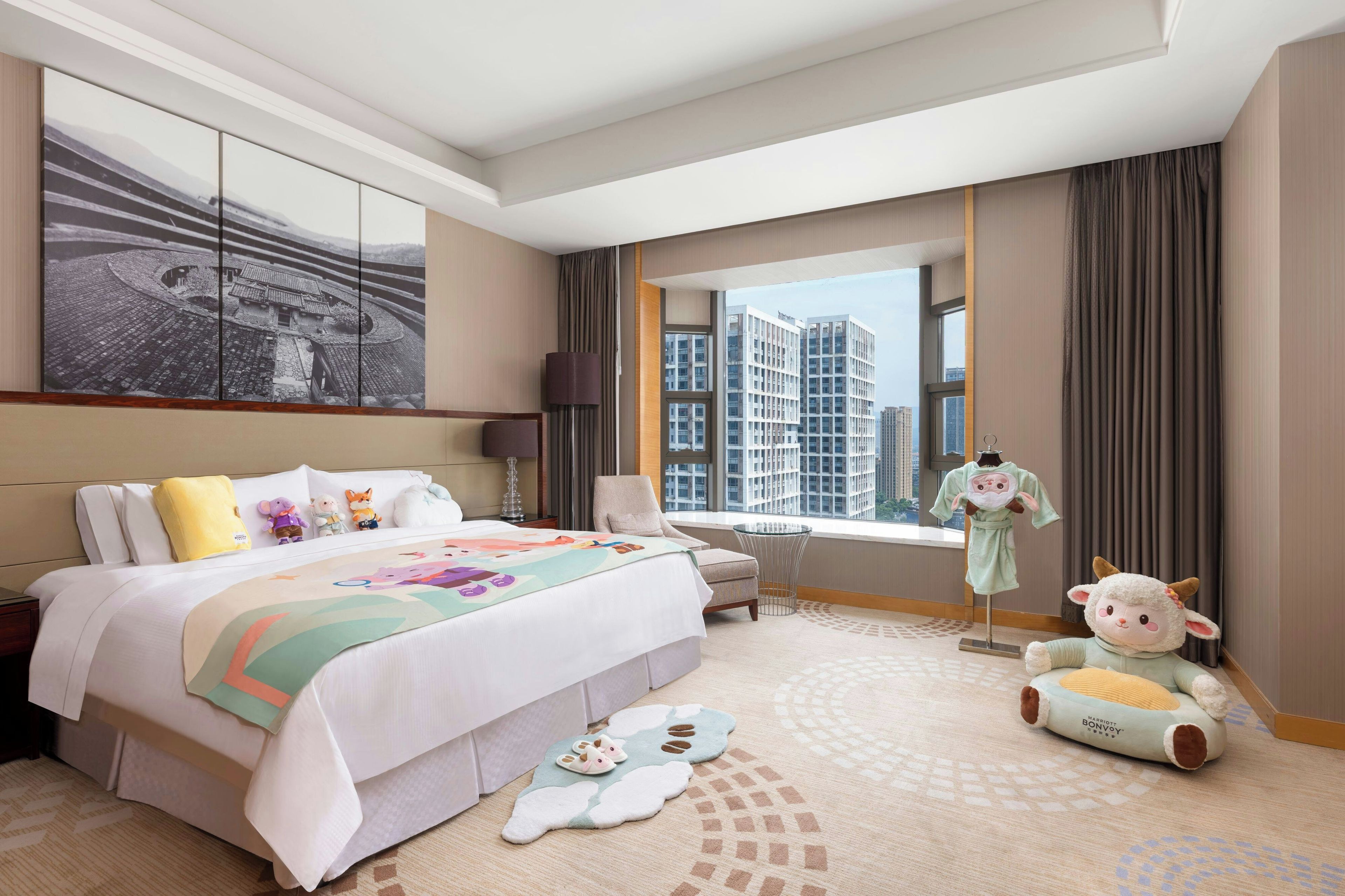 Camera d'albergo con un letto grande, una finestra vista città, una parete decorativa e un peluche sul pavimento.