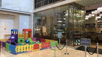 A children's play area with a colorful train set and a glass barrier in front of a restaurant.