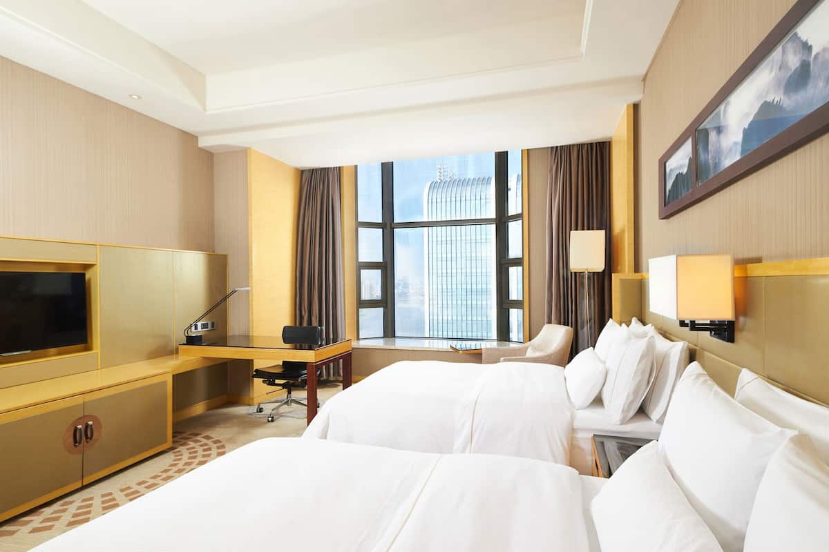 Ein Hotelzimmer mit einem großen Bett, einem Schreibtisch mit Stuhl, einem Fernseher und einem Fenster mit Vorhängen.