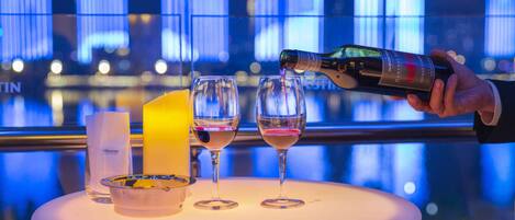 A hand pouring wine into glasses on a table with a cityscape view in the background.